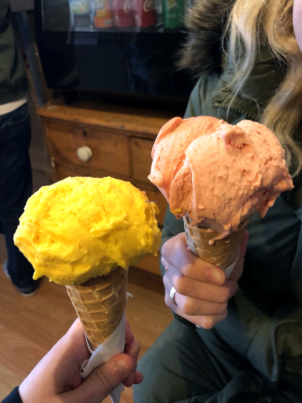 Two generous gelato cones — mango and strawberry — held up inside the shop